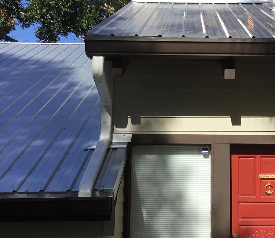 A downspout connects gutters at two different roof levels beside a house